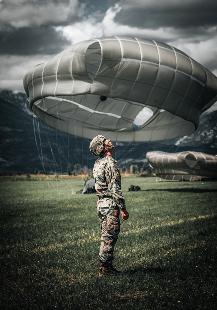 A US Army paratrooper assigned to the 173rd Airborne Brigade looks up as fellow paratroopers descend towards him during an airborne operation on Frida Drop Zone, Pordenone, Italy. The 173rd Airborne Brigade is the US Army's Contingency Response Force in Europe, providing rapidly deployable forces to the United States European, African and Central Command areas of responsibility. The brigade routinely trains alongside NATO Allies and partners.