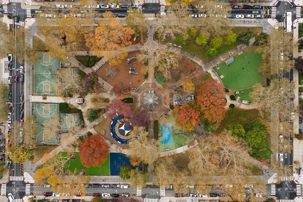 This aerial photograph presents a bird's-eye view of Church Square Park, Hoboken, New Jersey. The image captures the park's layout and diverse vegetation in the autumn season, showcasing a variety of colorful foliage.