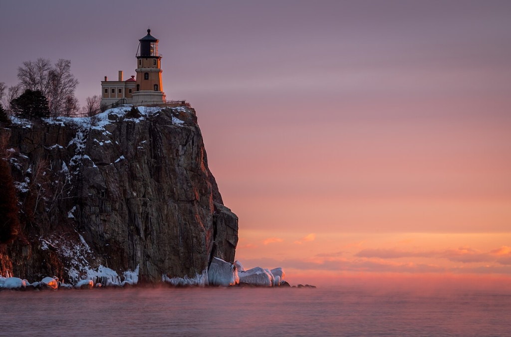 An early morning January photograph of the Split Rock Lighthouse, located near Two Harbors, Minnesota, on the shores of Lake Superior. The image captures the historic lighthouse perched atop a steep cliff, bathed in the soft pastel hues of dawn.